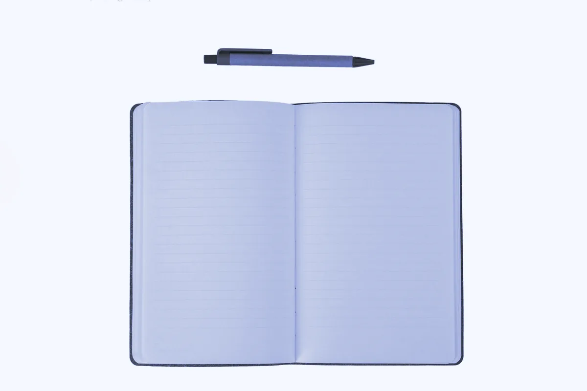 Libreta abierta con las hojas en blanco y un bolígrafo encima, sobre fondo blanco