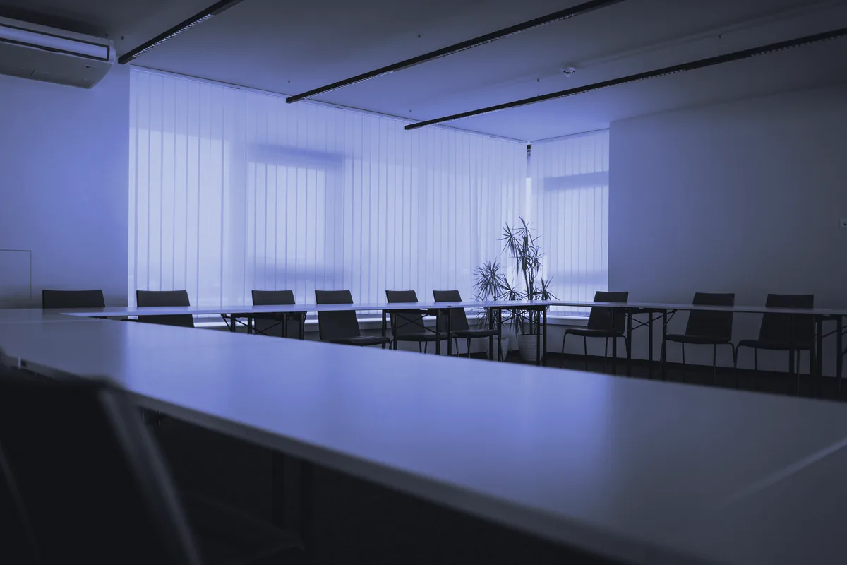 Sala de reuniones con mesas dispuestas en U y cortinas verticales en las ventanas