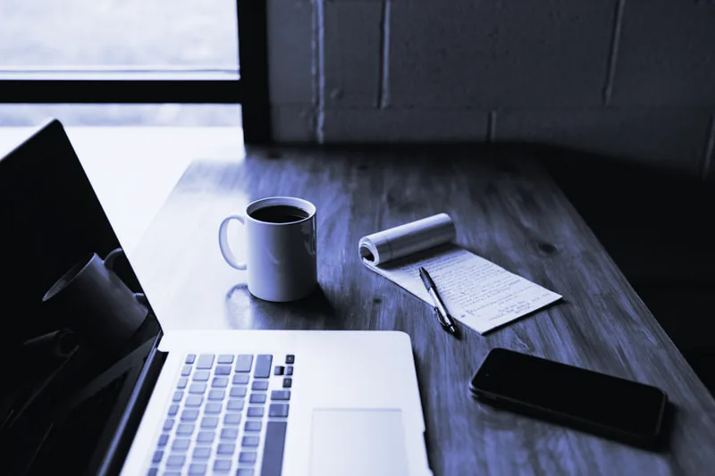 Portátil, taza de café, libreta y móvil sobre una mesa de madera