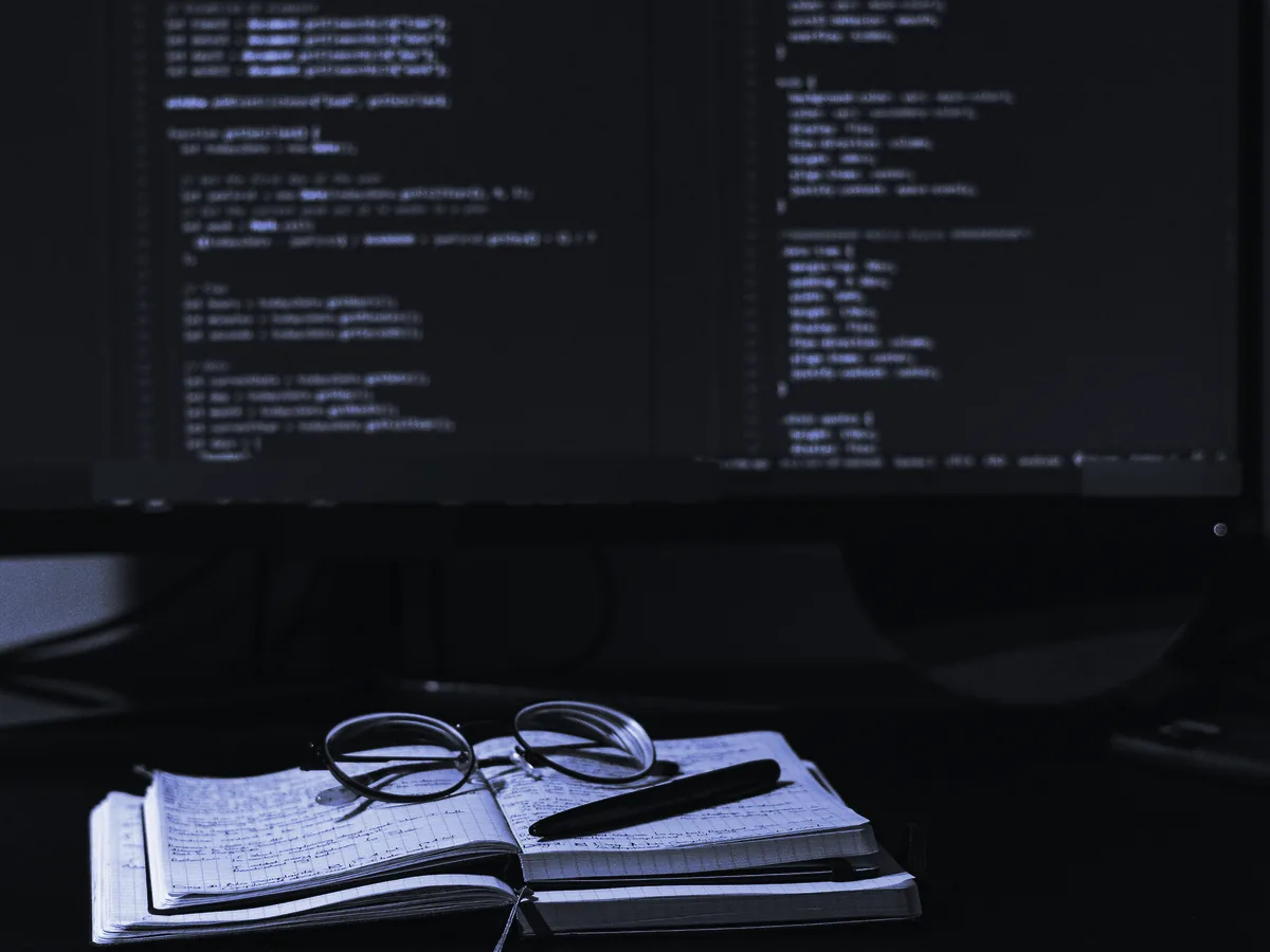 Monitor con código y un cuaderno abierto con unas gafas encima