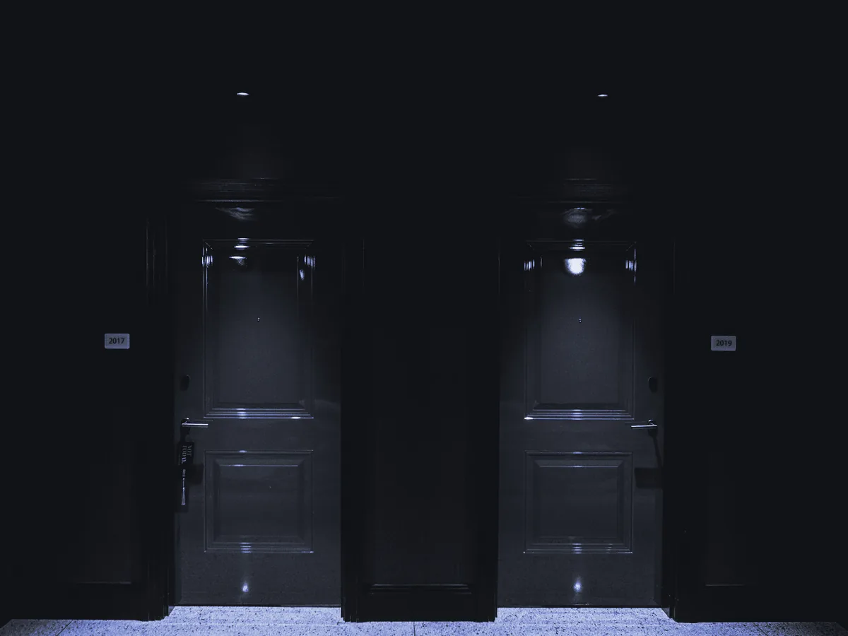 Dos puertas iguales, una junto a otra, en un pasillo a oscuras