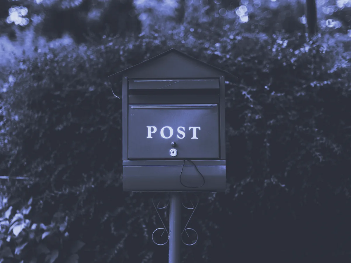 Buzón con la palabra «POST» sobre un poste, delante de un seto