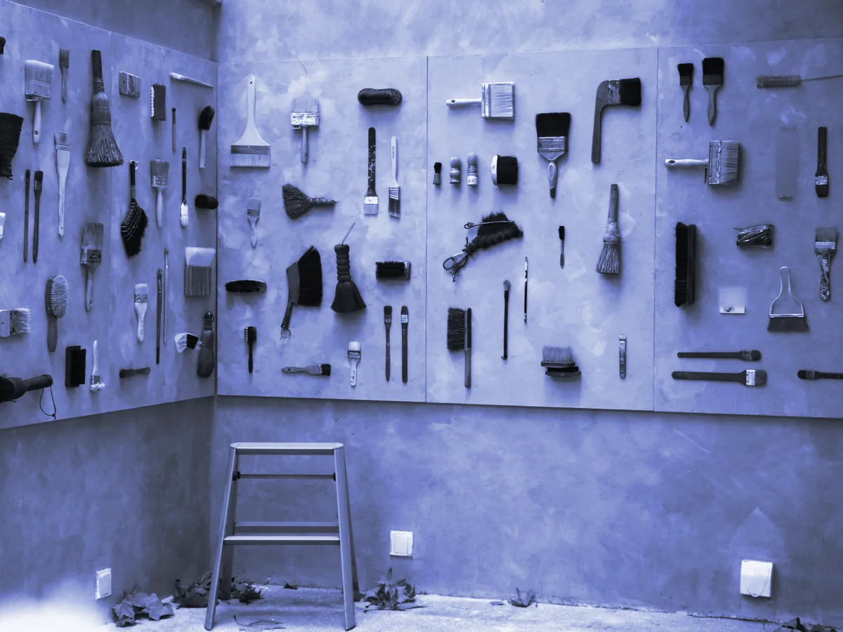 Pared con brochas y cepillos colgados en orden y una escalera de mano