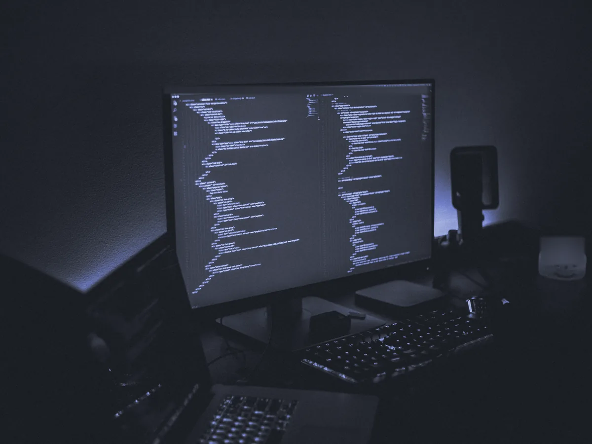 Monitor con código sobre un escritorio a oscuras, con un teclado delante