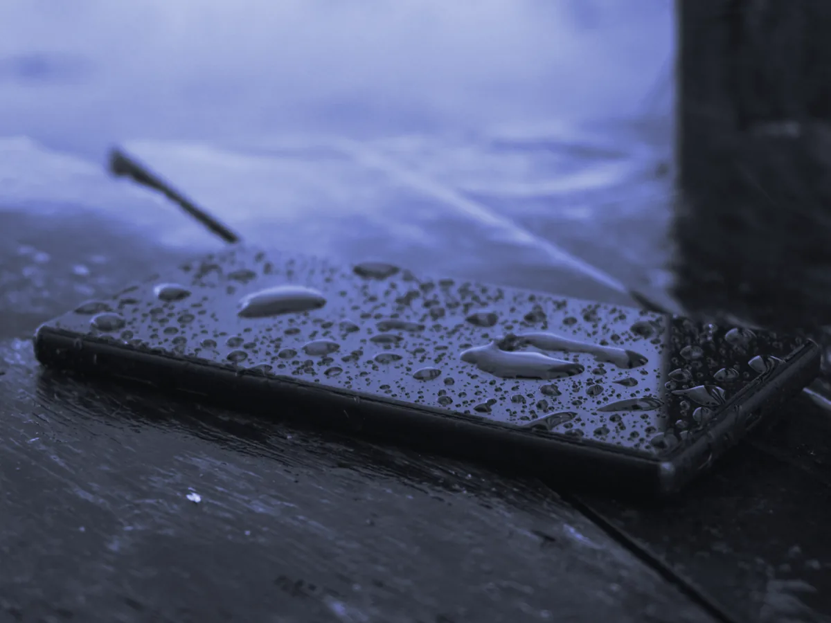 Móvil negro cubierto de gotas de agua sobre una mesa de madera
