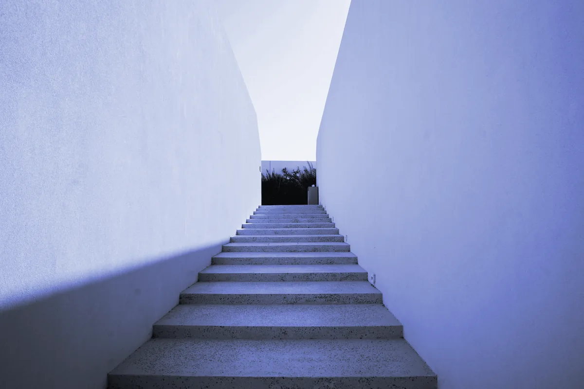 Escalera exterior de hormigón entre dos muros altos, que sube hacia el cielo
